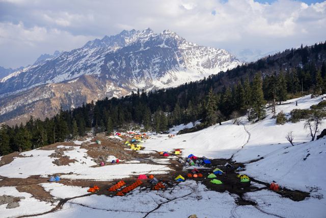 Colourful tents pitched on a snowy Himalayan ridge below a snow peak