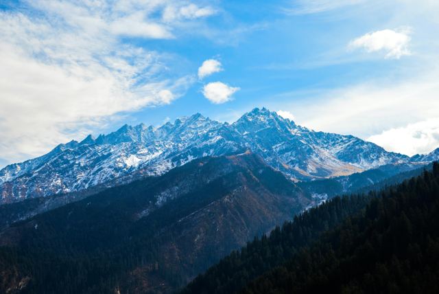 Snow-capped Himalayan peak above forested valleys under a blue sky