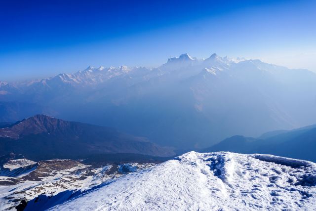 Snowy ridge in the foreground with a Himalayan range fading into haze