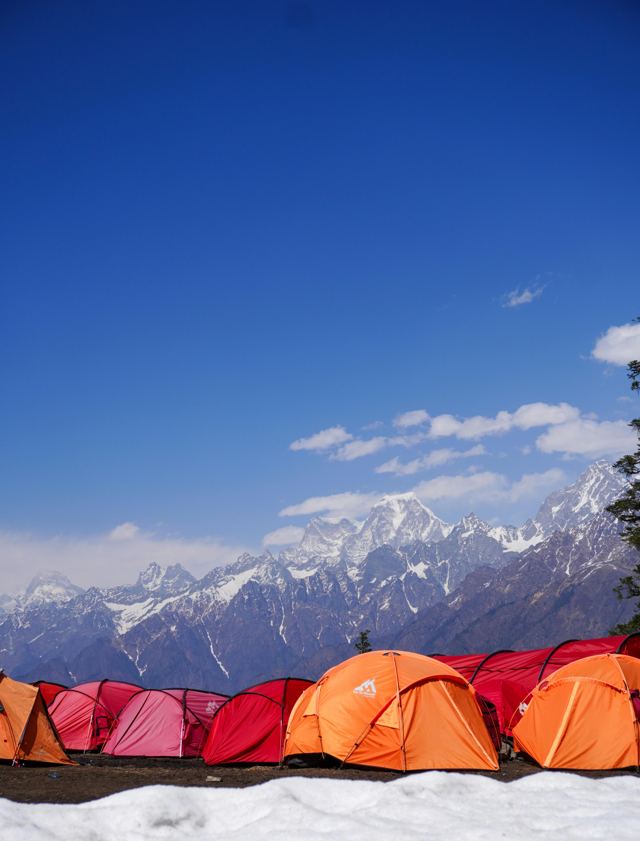 Orange and red tents at a trek campsite under a deep blue sky